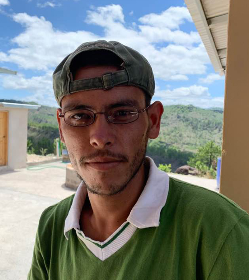 Man in Guatemala wearing new eyeglasses, standing outdoors with mountains in the background.