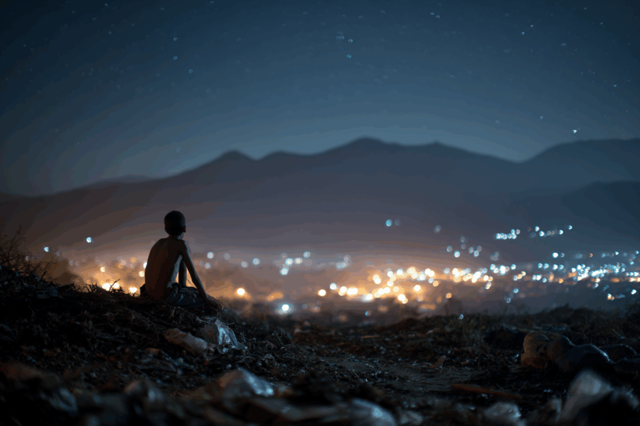 A young boy standing on a trash dump, gazing up at the night sky filled with stars – inspired by a real mission story from Bryan Kaiser’s They Shall See God.